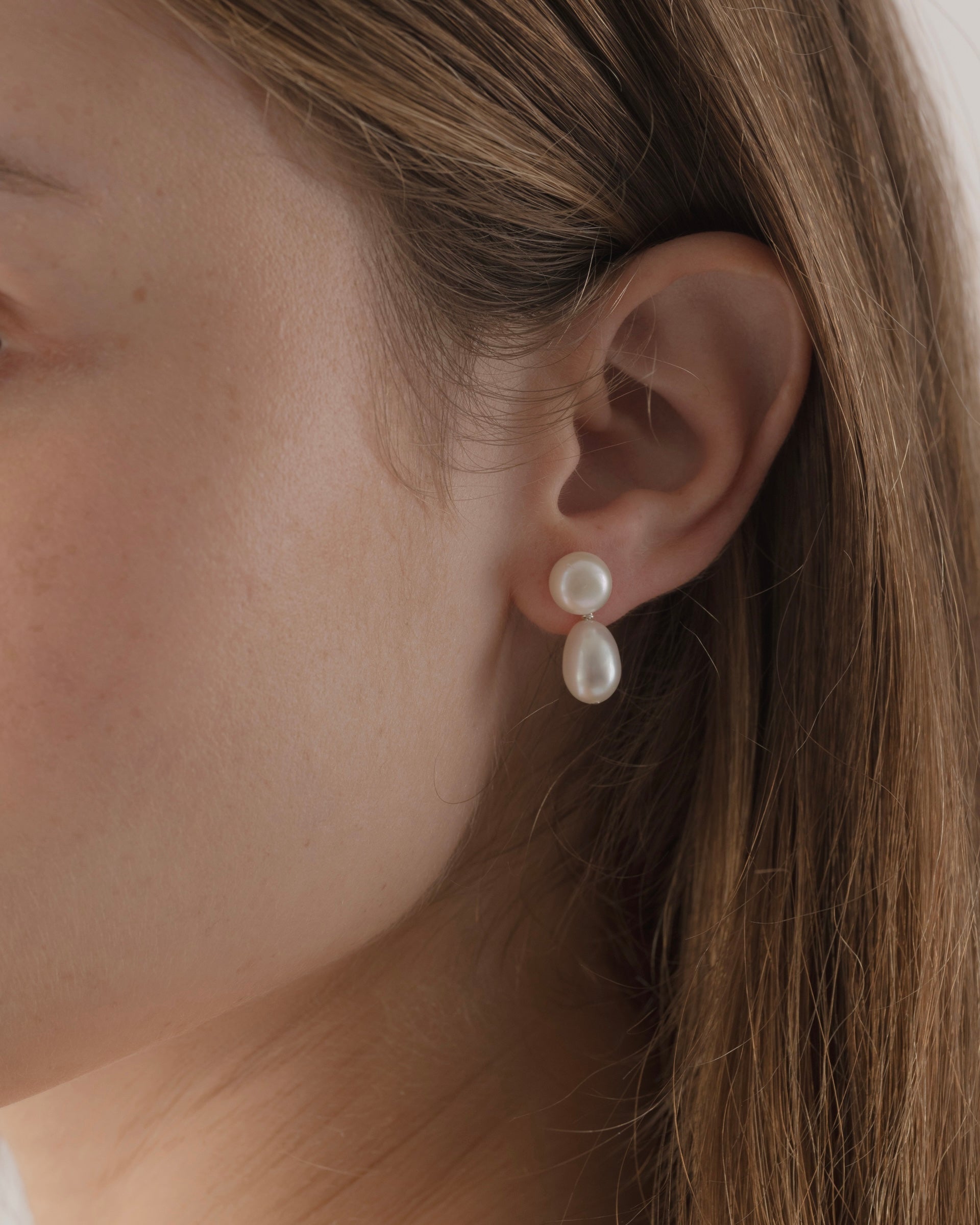 Pearl earring worn by a person with light skin and brown hair.