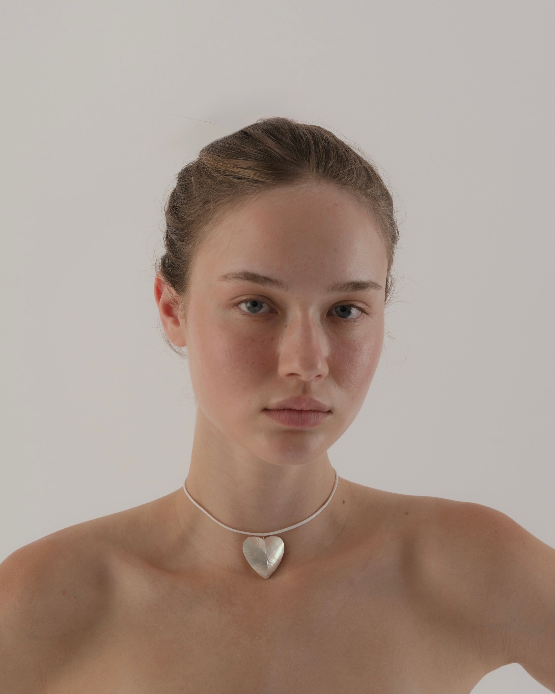 Woman wearing a heart-shaped silver necklace against a plain background