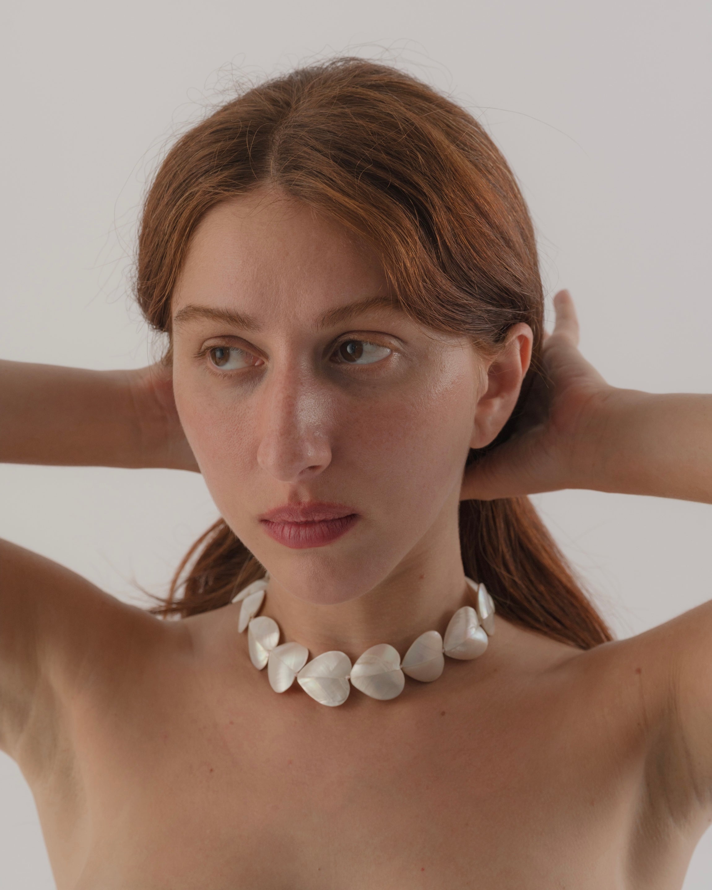 Woman wearing a white necklace against a plain background