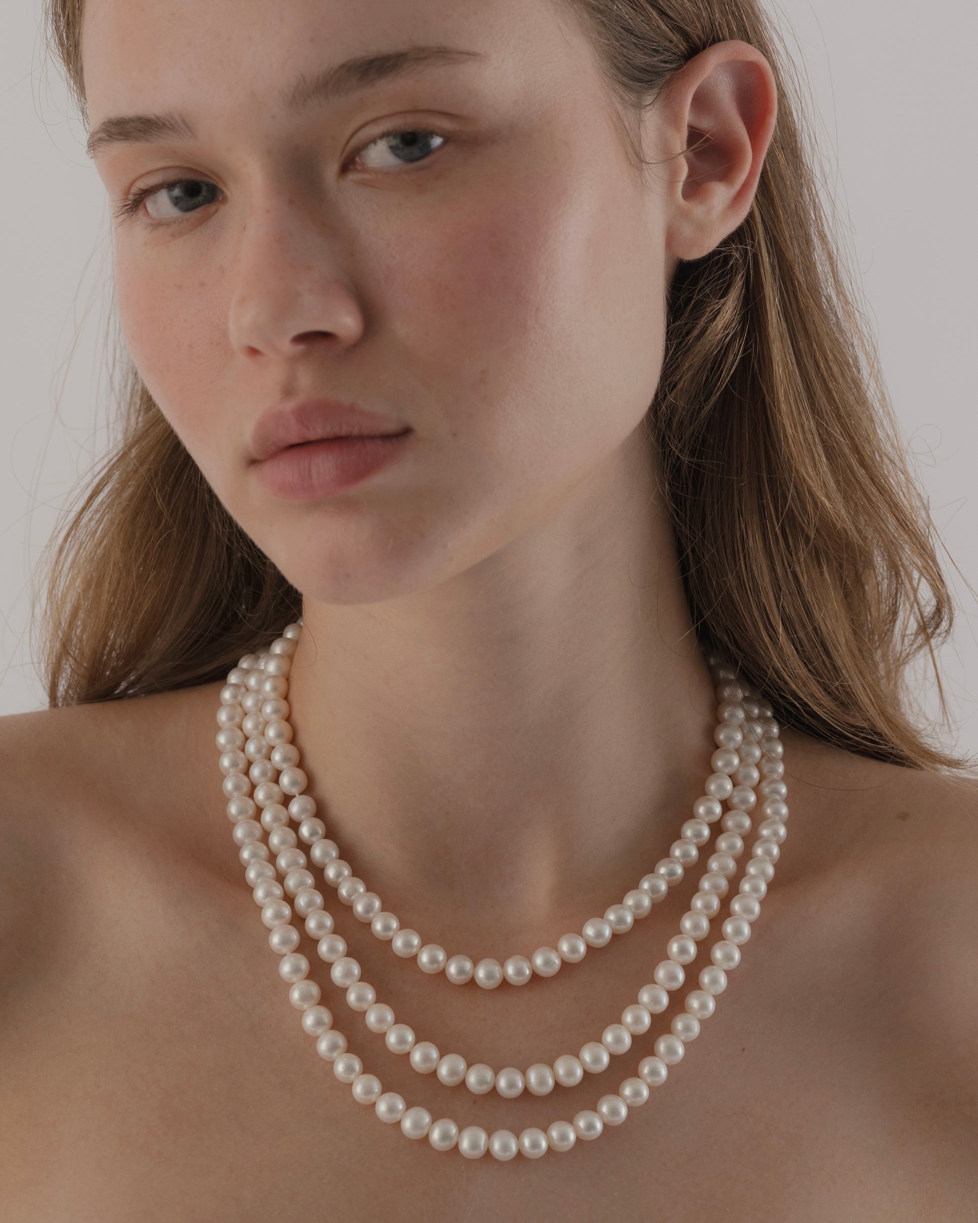 Woman wearing a pearl necklace against a neutral background