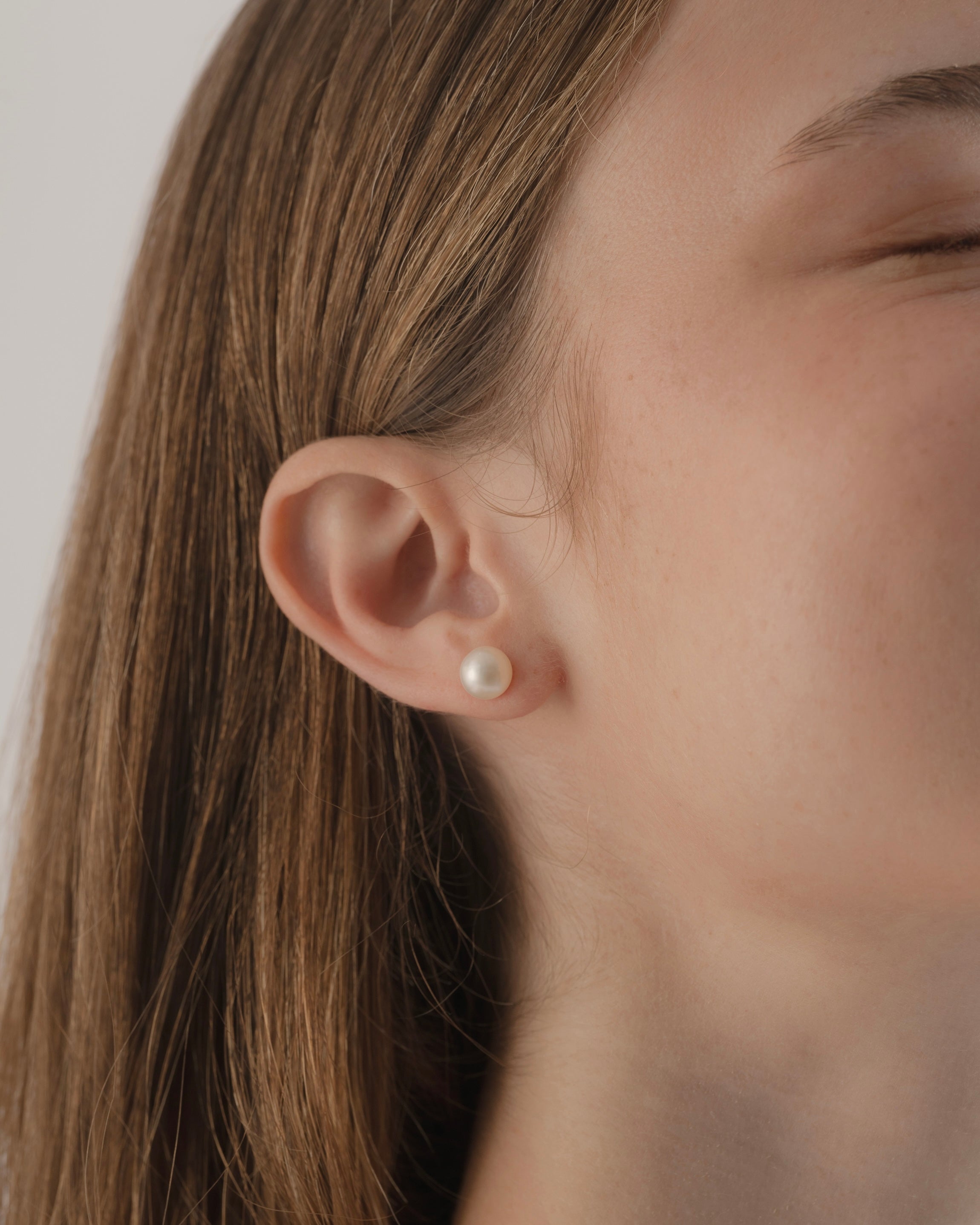 Close-up of a person wearing a pearl earring with a neutral background