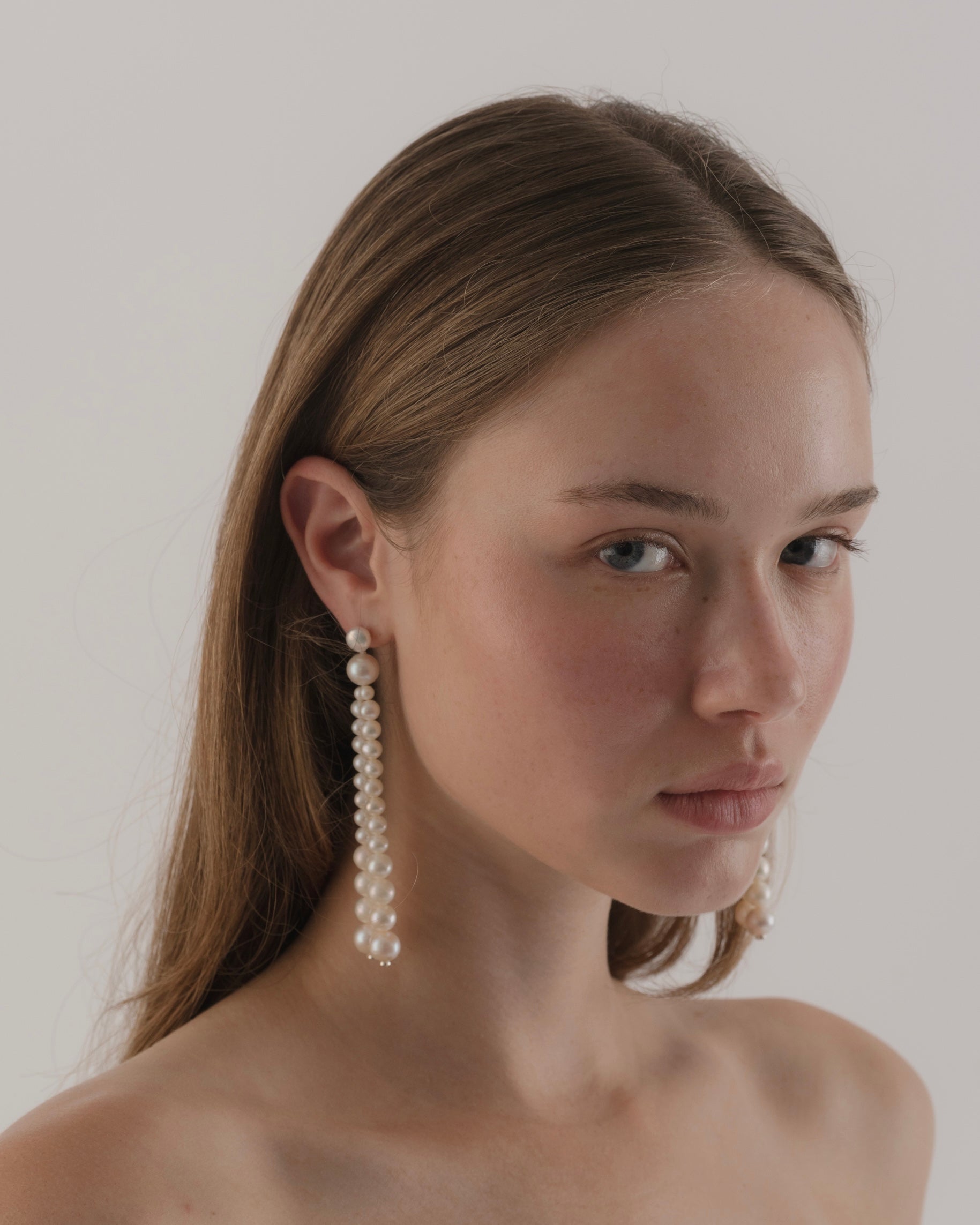Woman wearing pearl earrings against a plain background