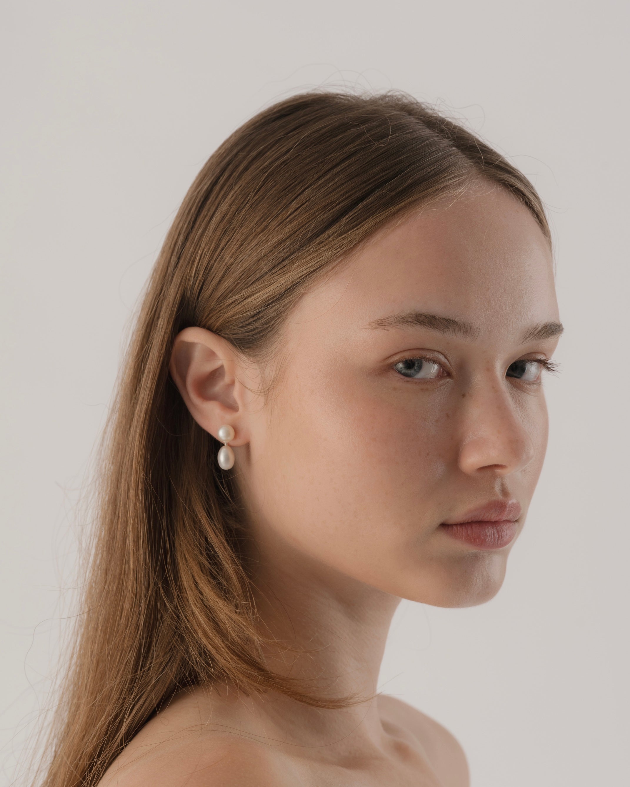 Woman wearing pearl earrings against a plain background