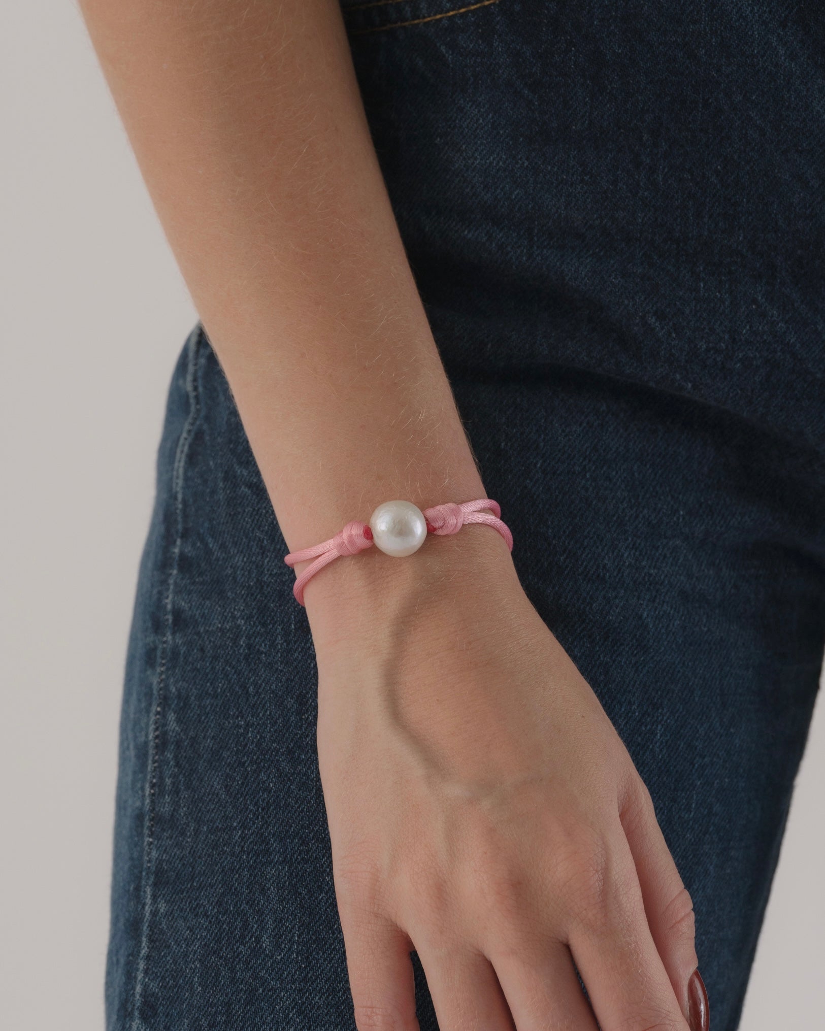 Pink bracelet with a pearl on a wrist against a dark denim background
