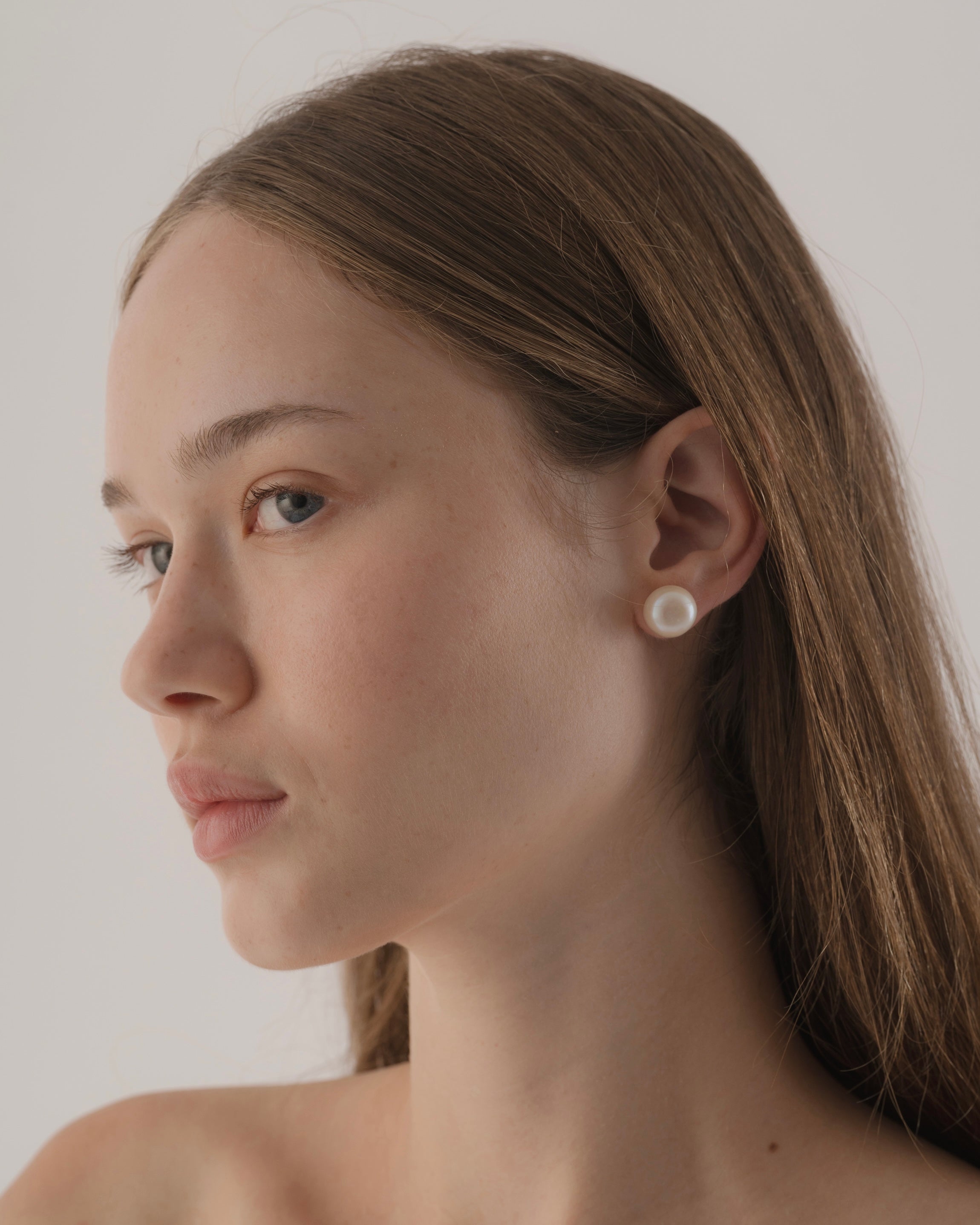 Close-up of a woman wearing pearl earrings against a plain background