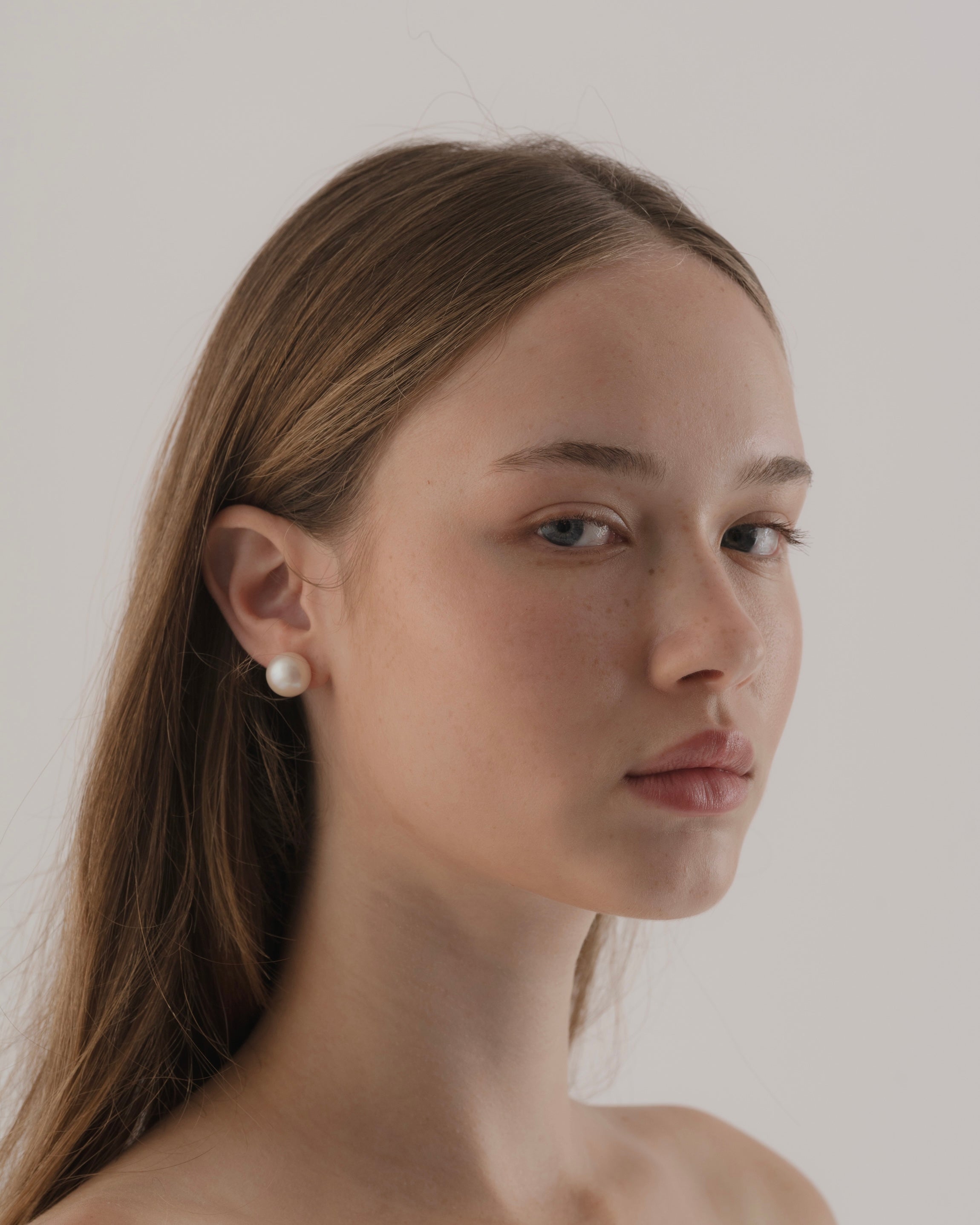 Woman wearing a pearl earring against a plain background