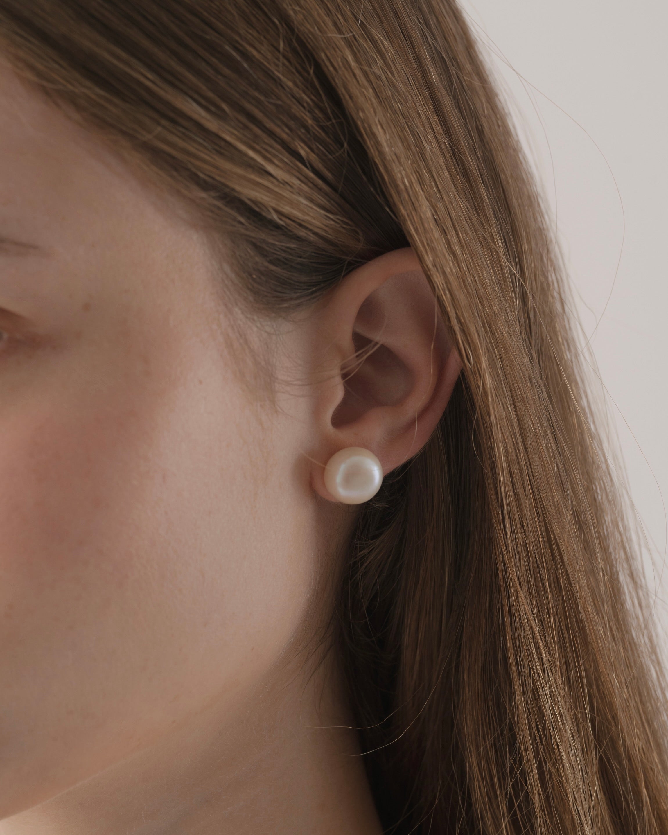 Close-up of a person wearing a pearl earring with a neutral background