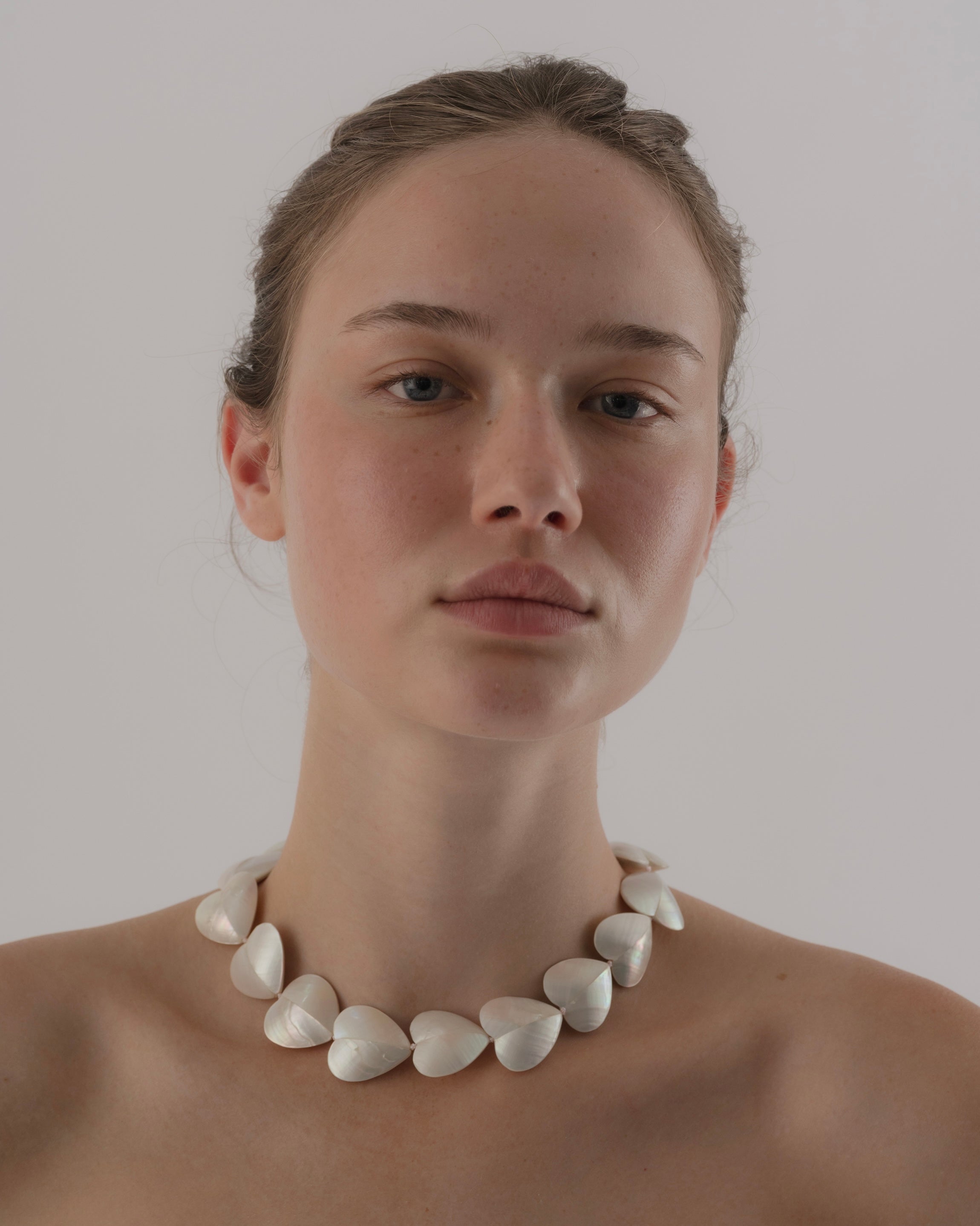 Woman wearing a white heart-shaped necklace against a plain background