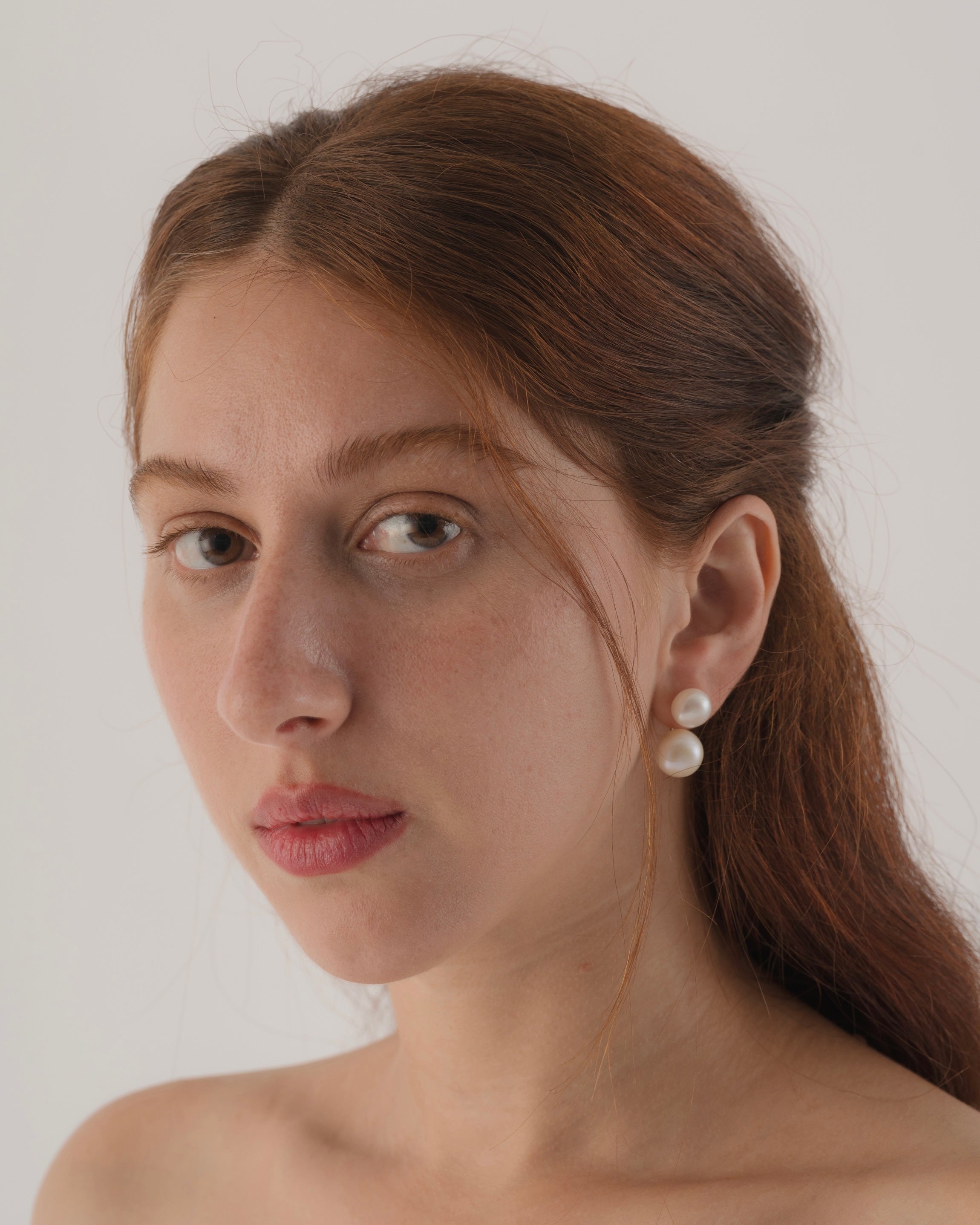 Woman wearing pearl earrings against a plain background