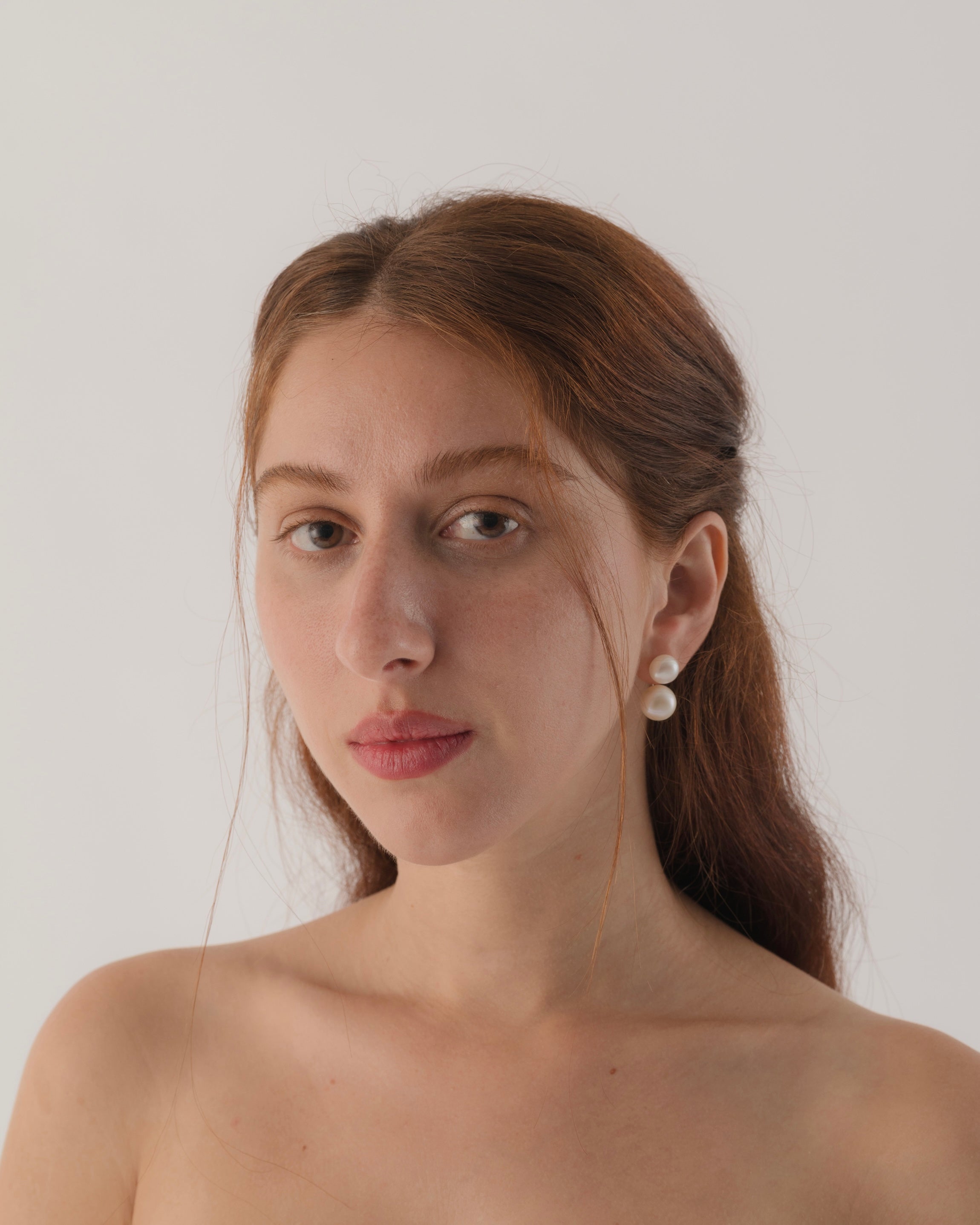 Woman wearing pearl earrings against a plain background