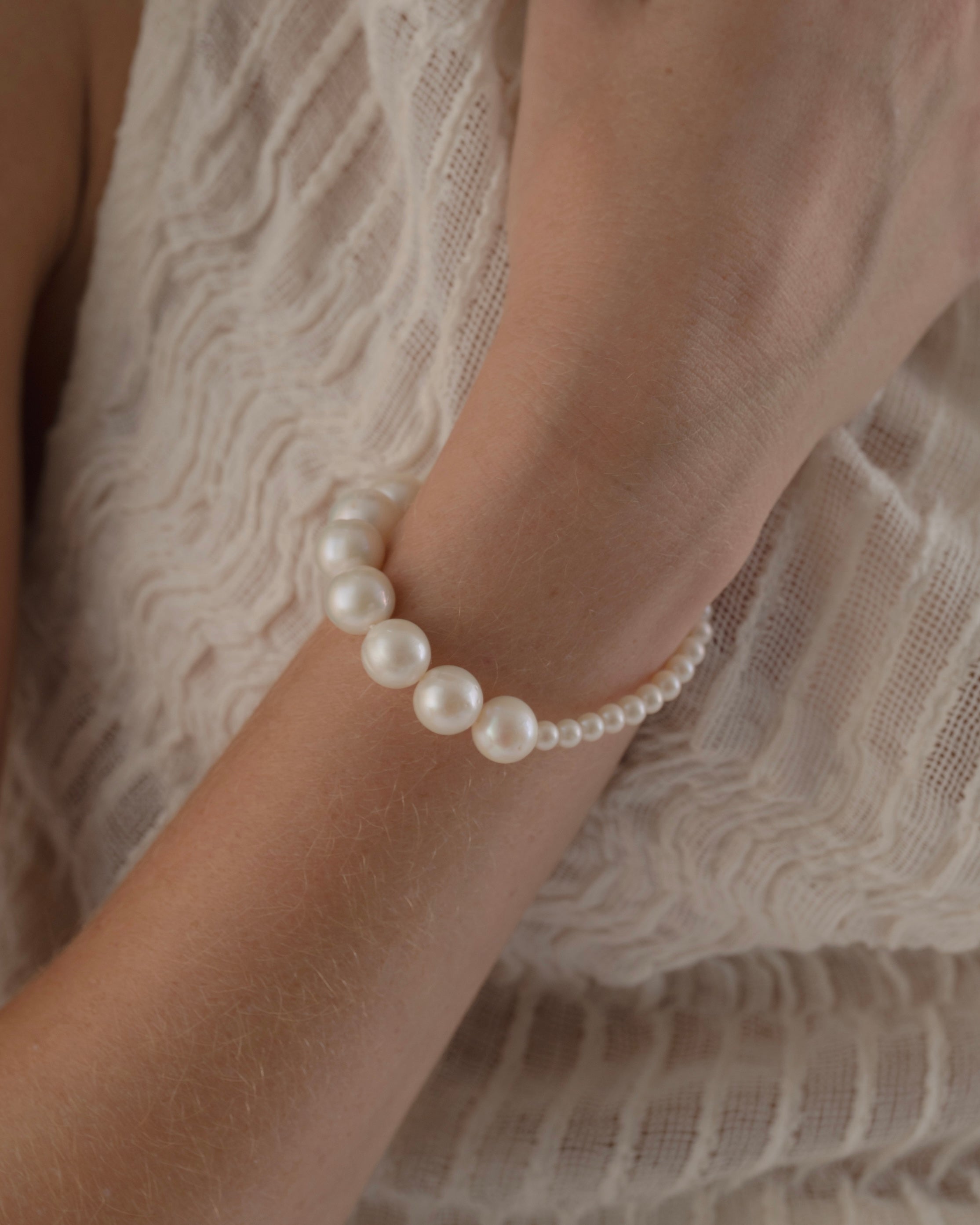 Pearl bracelet on a wrist with a lace garment in the background