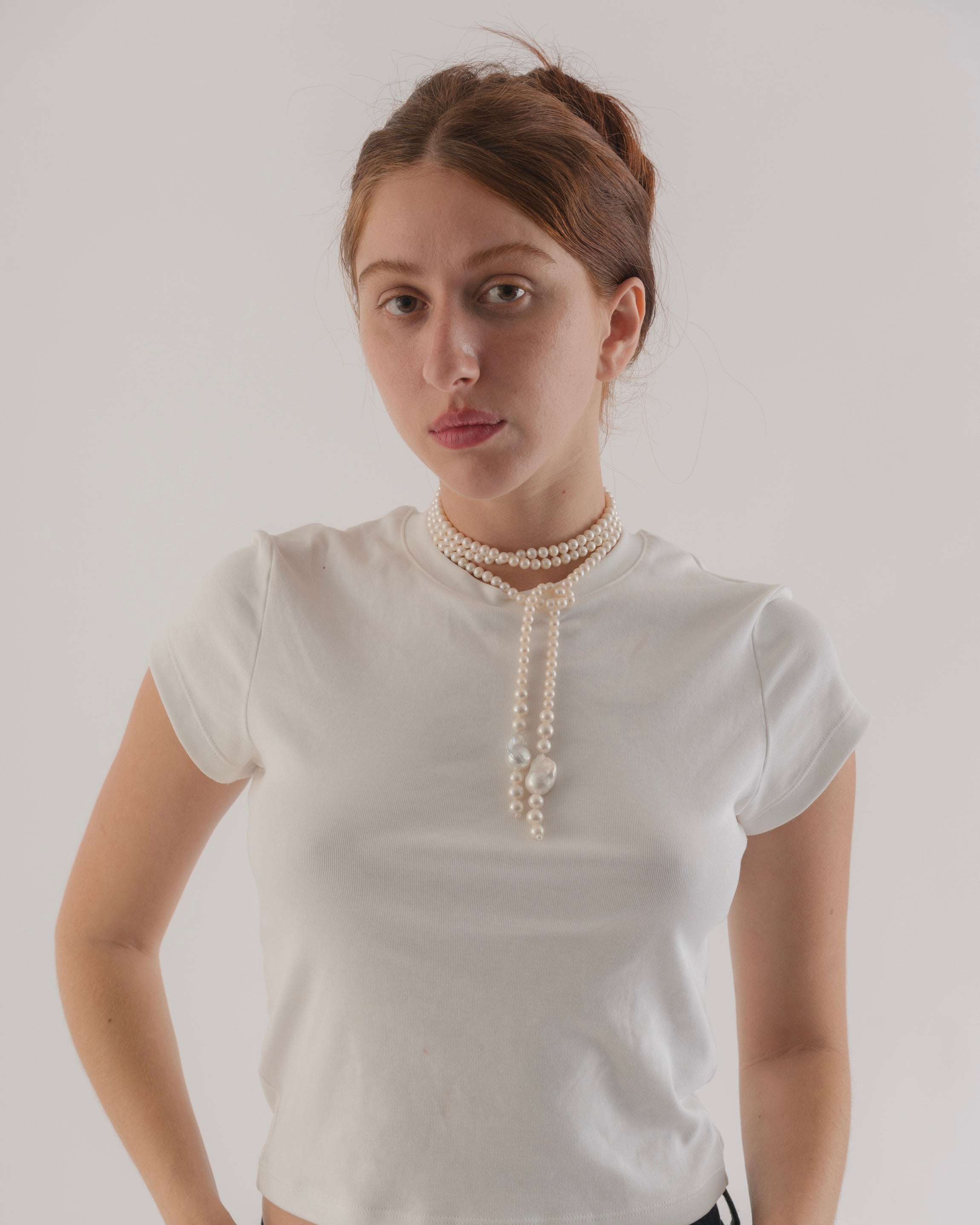 Woman wearing a white t-shirt with a long pearl necklace against a plain background