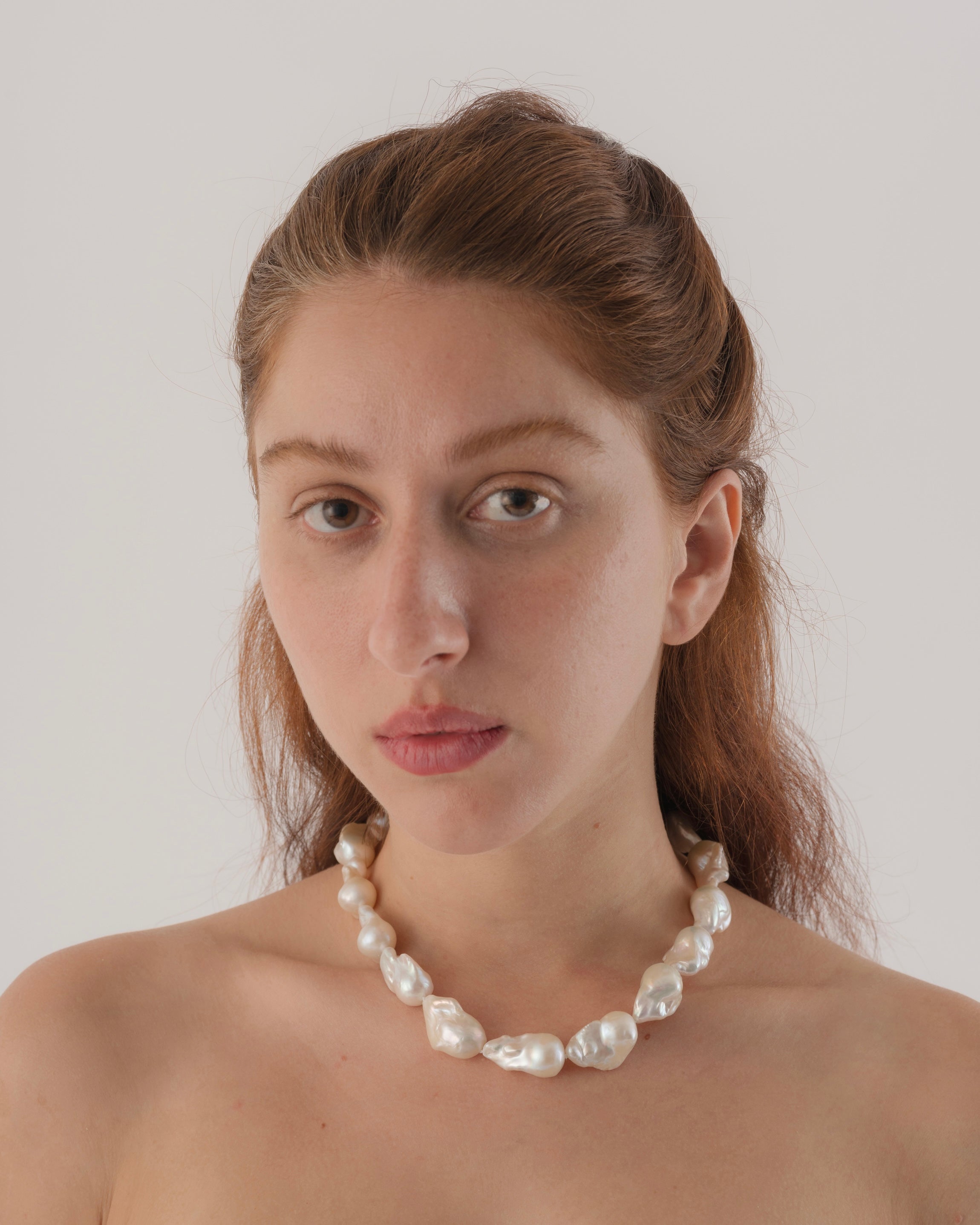 Woman wearing a pearl necklace against a plain background