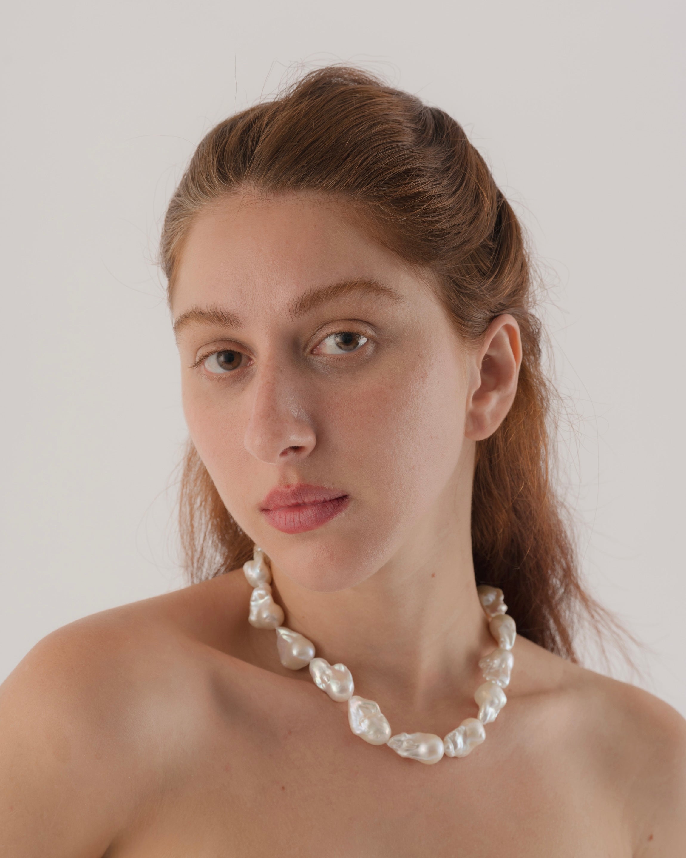 Woman wearing a pearl necklace against a plain background