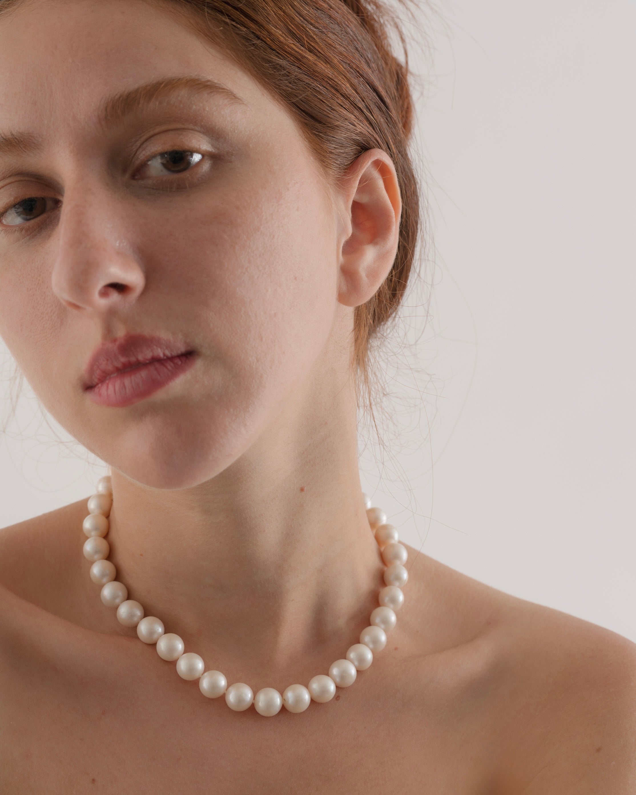Woman wearing a pearl necklace against a plain background