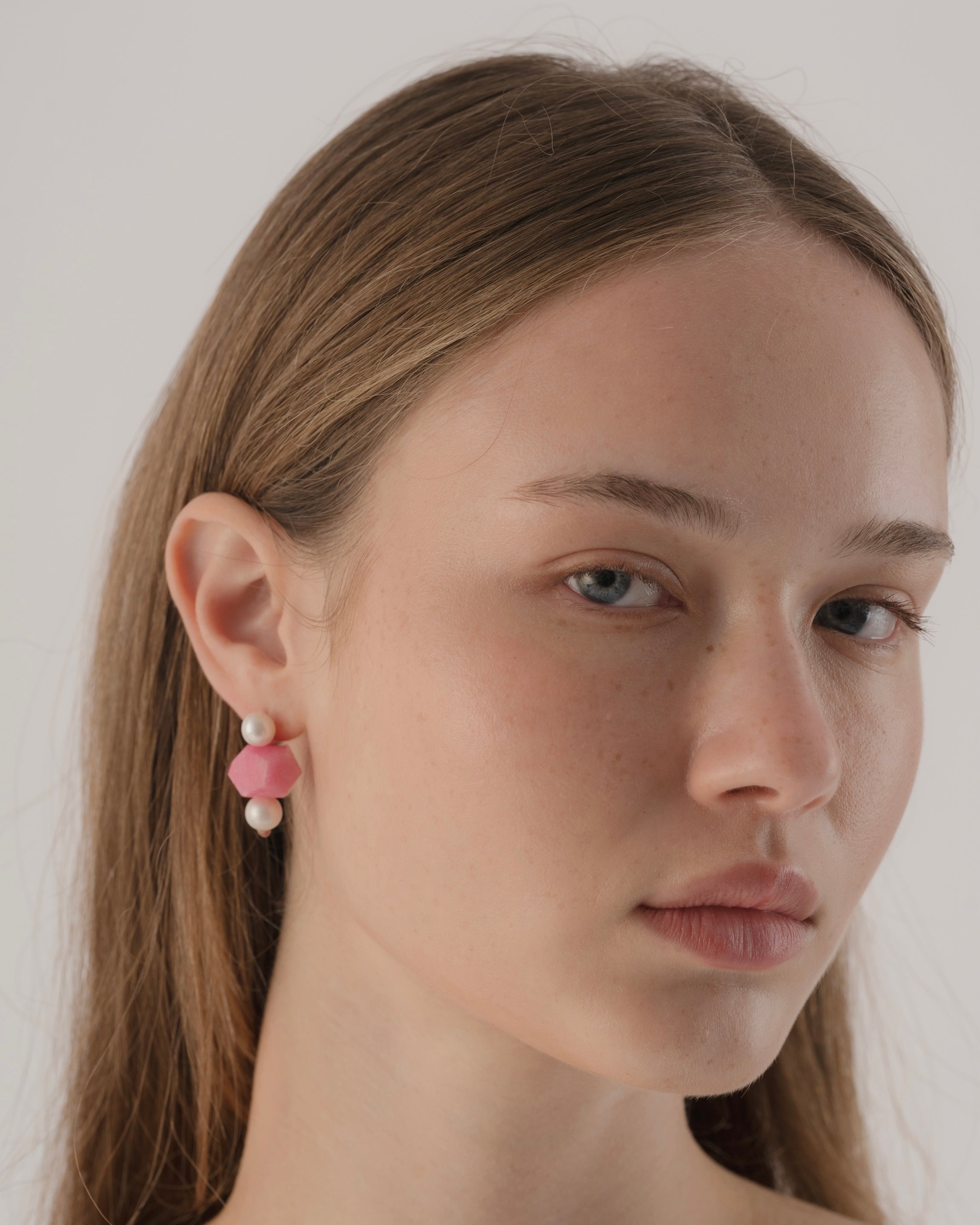 Close-up of a person wearing pink earrings with a plain background