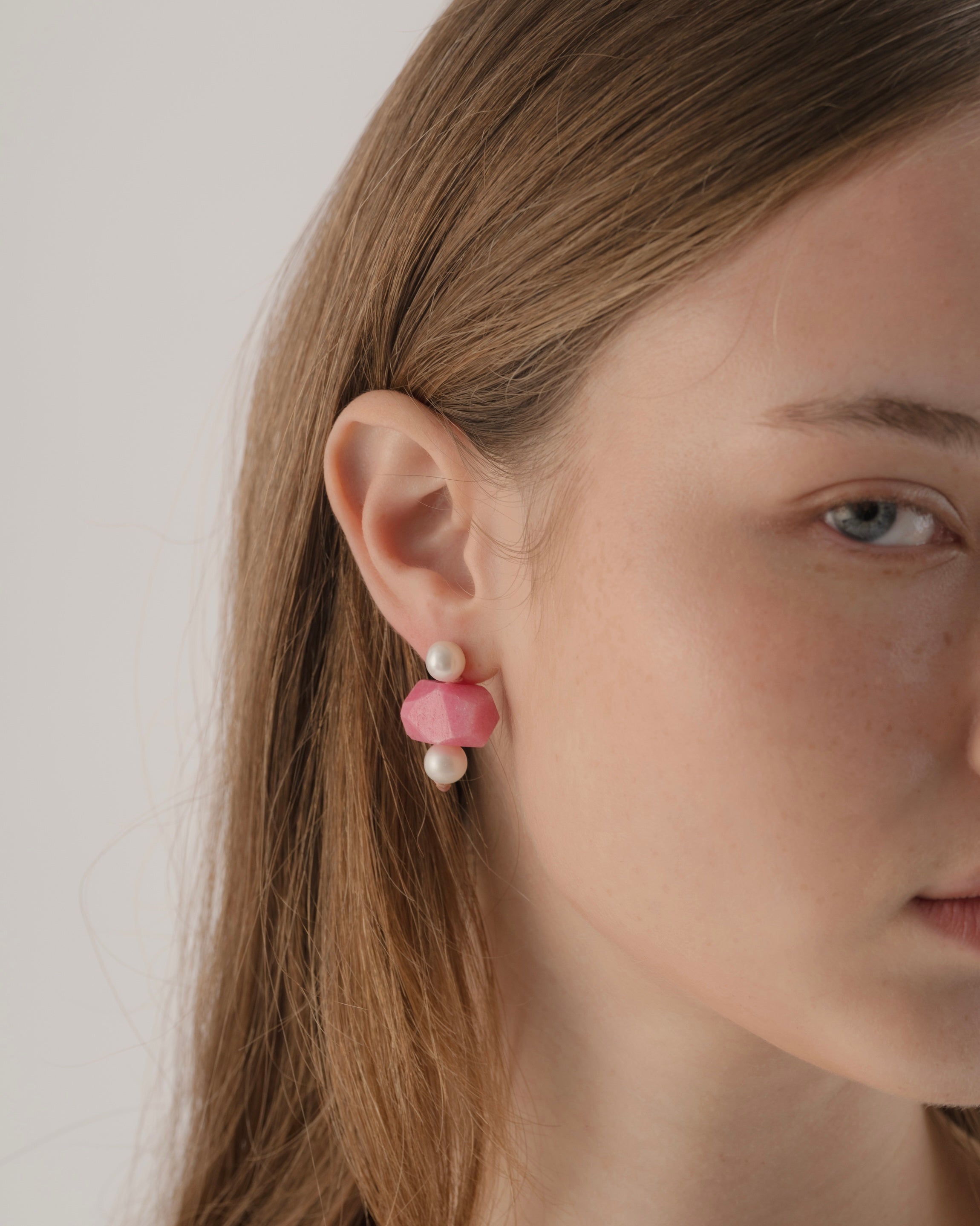 Close-up of a person wearing pink earrings with pearls against a neutral background