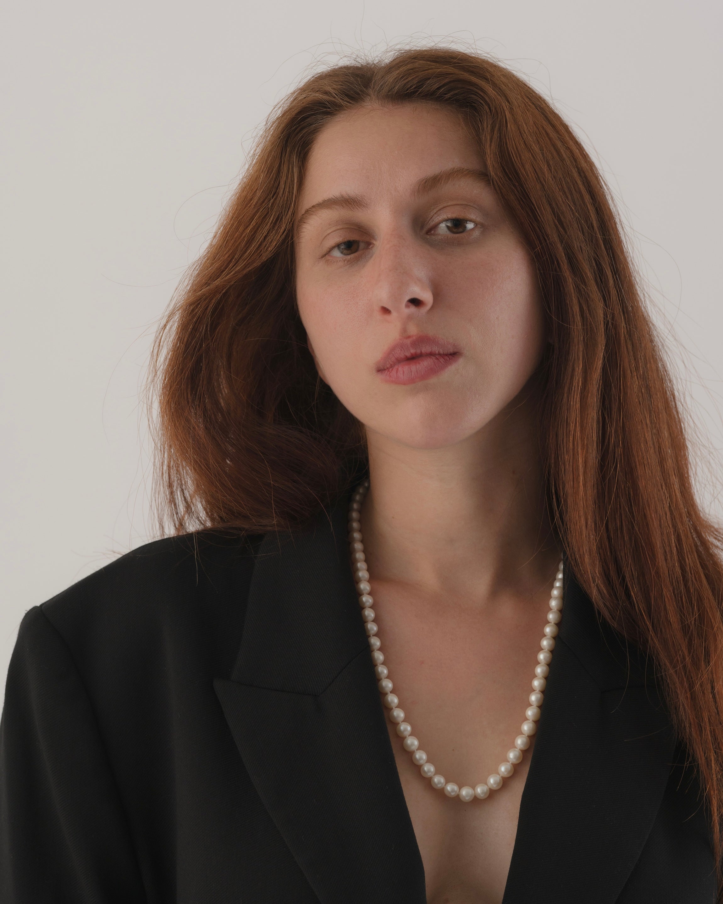 Woman wearing a black blazer and pearl necklace against a plain background