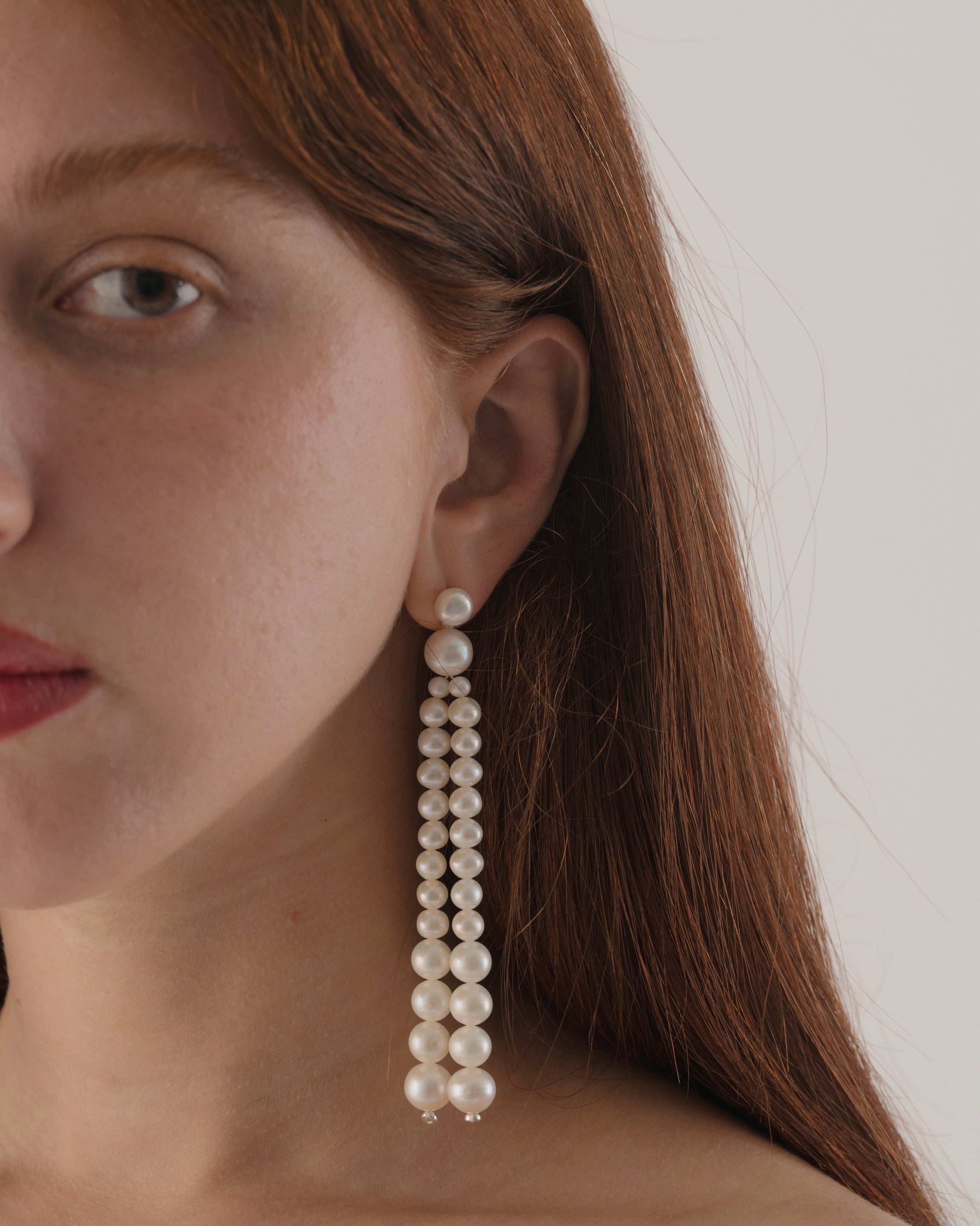 Close-up of a person wearing pearl earrings with a neutral background