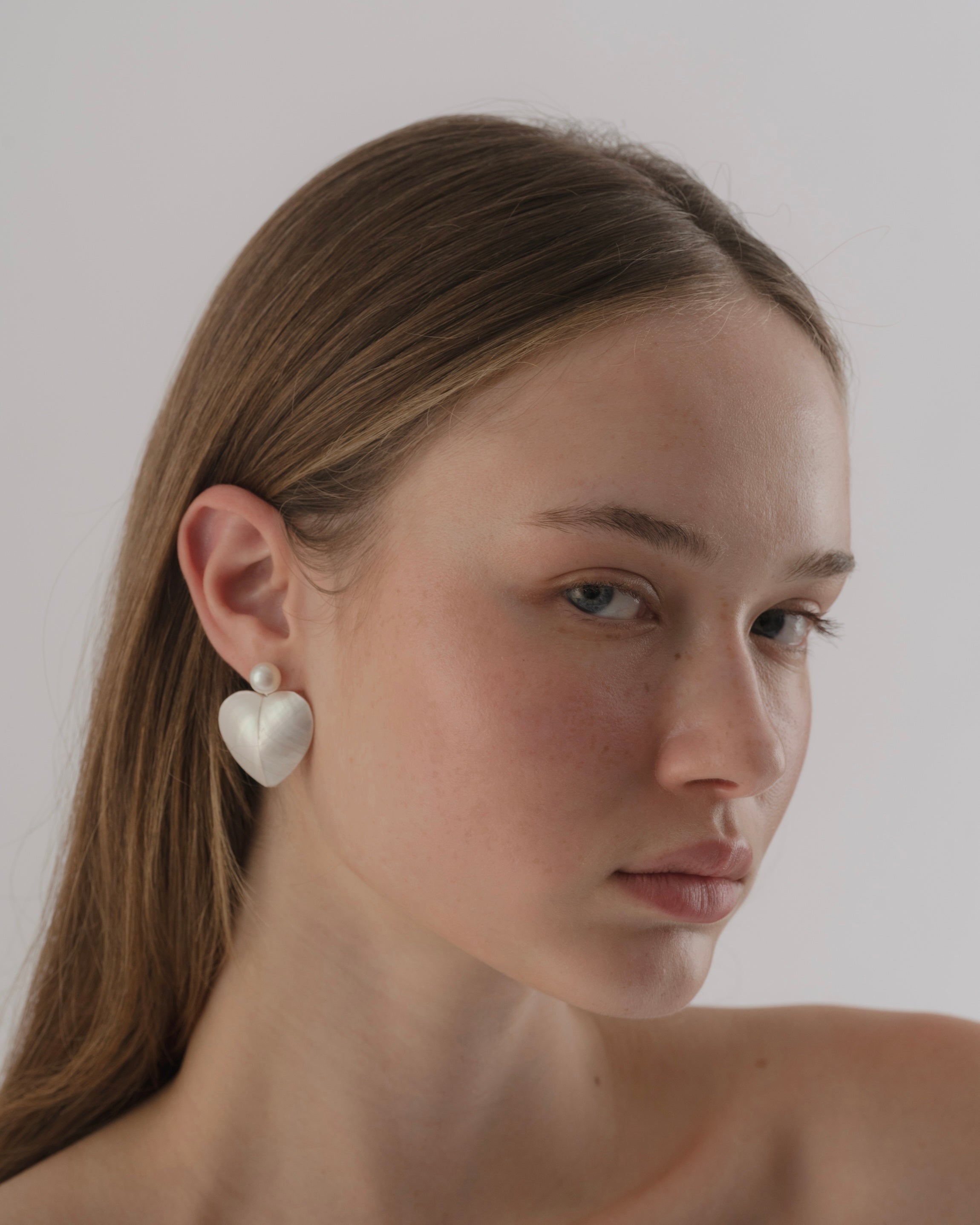 Woman wearing heart-shaped earrings against a plain background