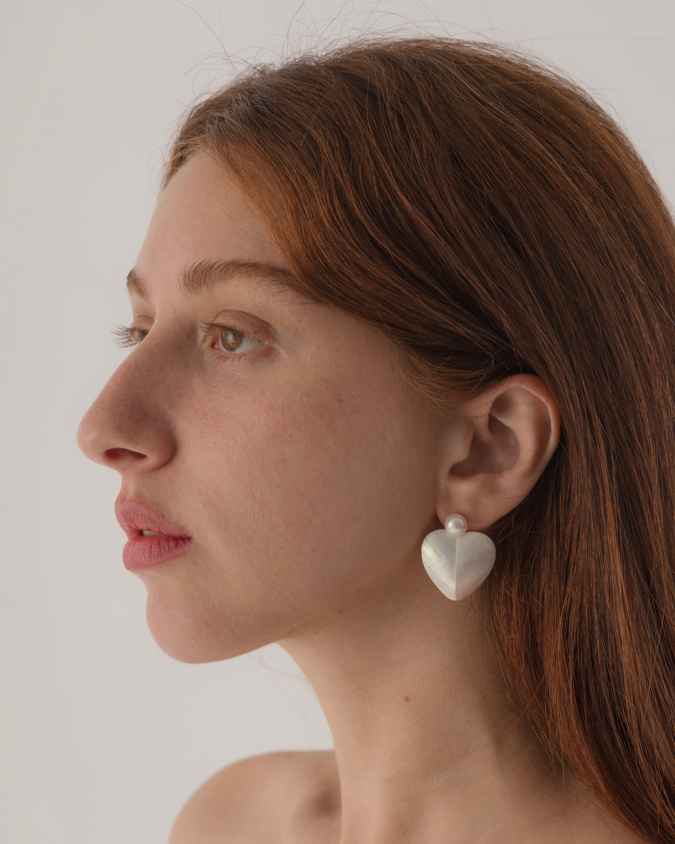 Close-up of a woman wearing heart-shaped earrings against a plain background