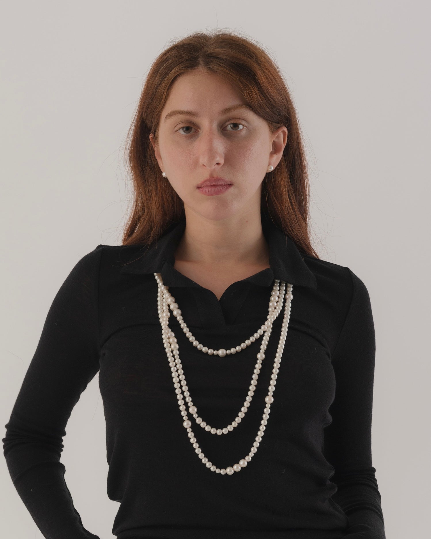 Woman wearing a black top and multiple pearl necklaces against a white background