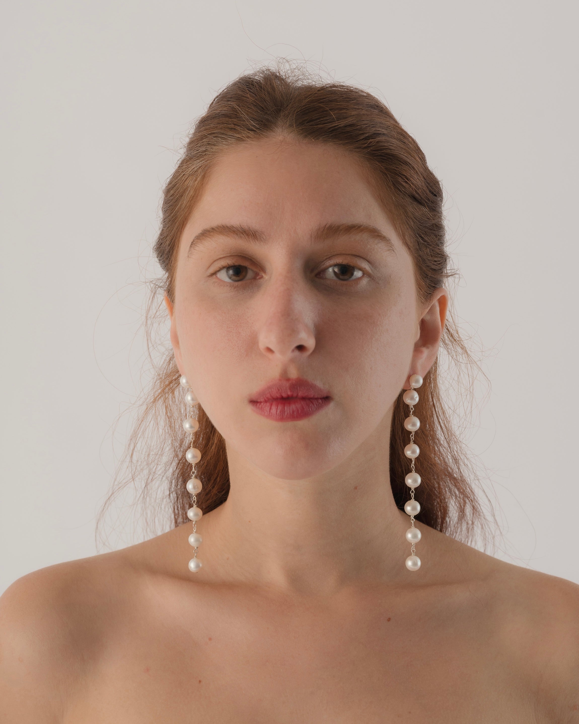 Woman wearing pearl earrings against a plain background