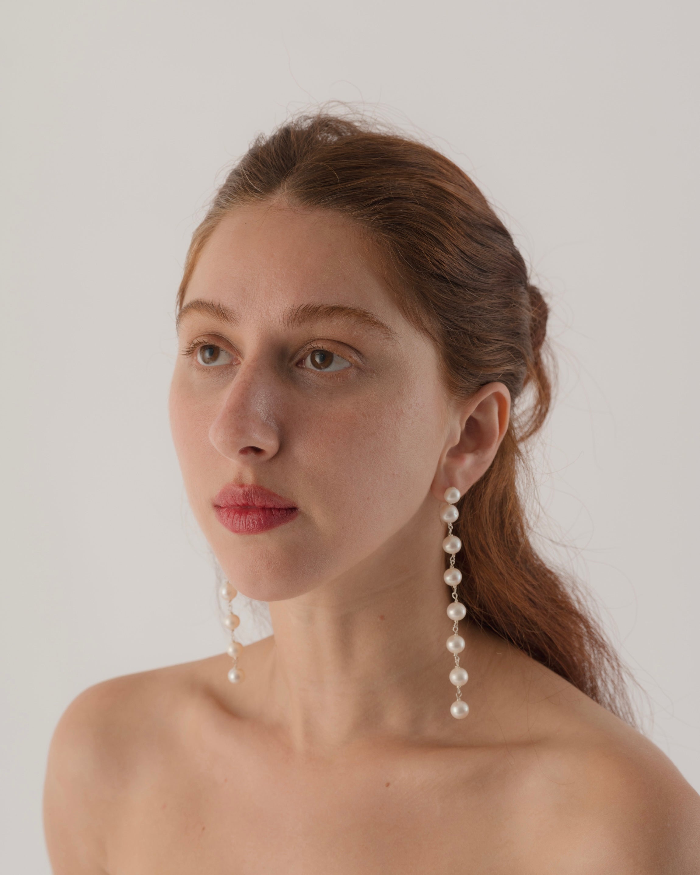 Woman wearing pearl earrings against a plain background