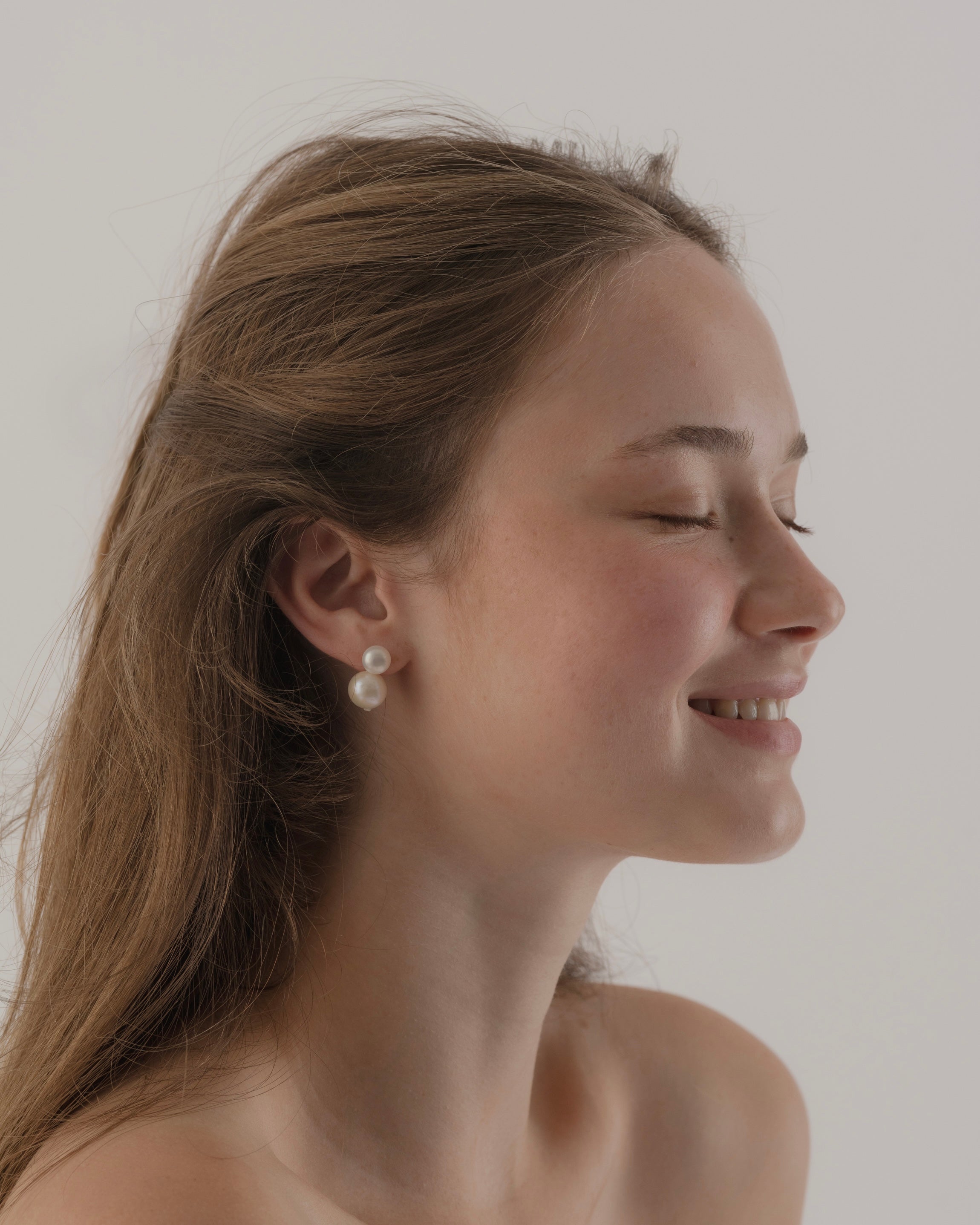 Woman wearing pearl earrings with a neutral background
